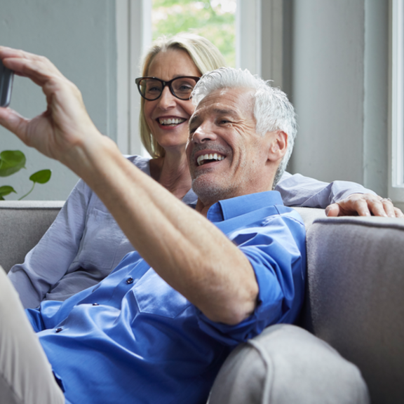 Happy mature couple sitting on couch at home taking a selfie